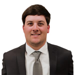Smiling man in a suit with a light gray tie against a white background. Formal attire headshot.