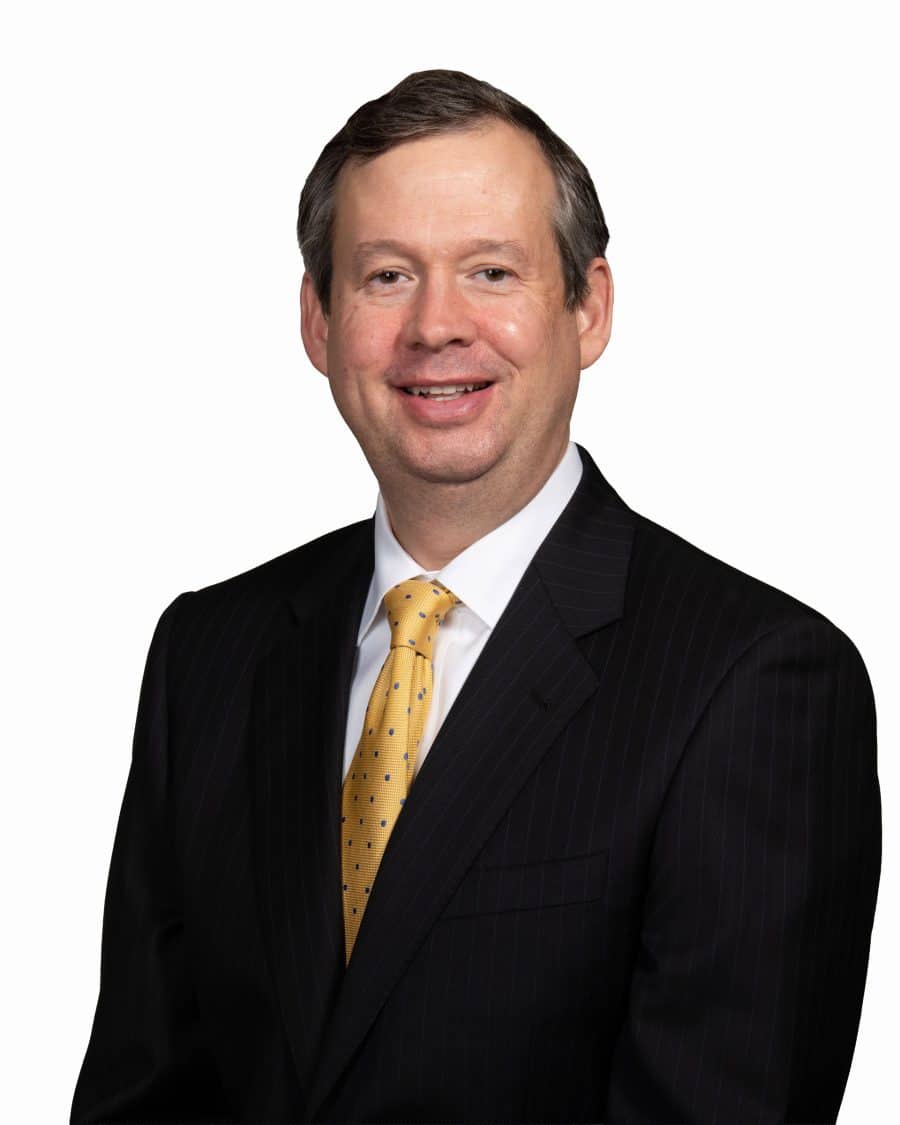 Businessman in a suit and yellow tie smiling against a white background, professional portrait.