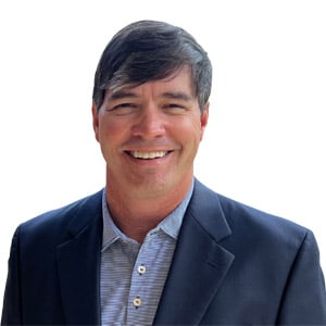 A man in a dark blazer smiles at the camera against a plain white background.