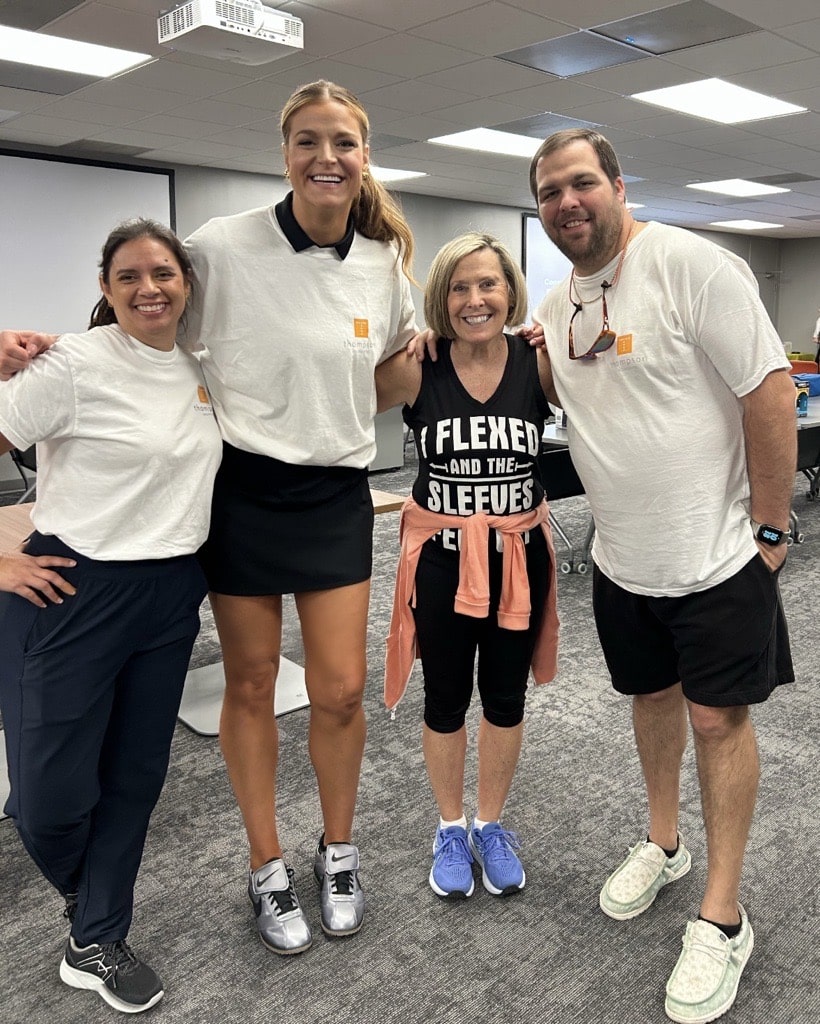Group of four people smiling and posing indoors at a casual event, wearing relaxed athletic attire.