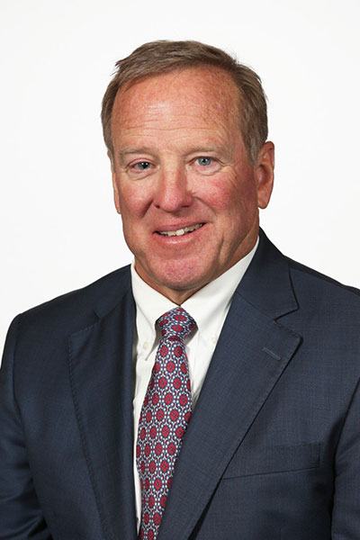 Businessman in a suit and patterned tie posing against a plain background.