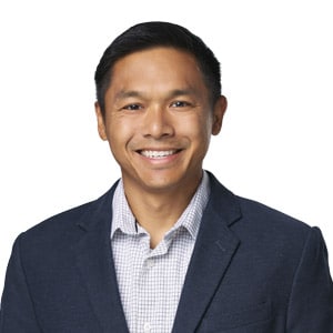 Smiling man in a suit jacket against a white background, suitable for professional or business contexts.