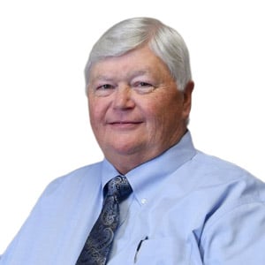 Elderly man in a blue shirt and tie, smiling against a white background.