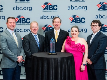 Group of professionals posing with an award at an ABC.org event backdrop, celebrating achievement.