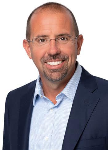 Smiling person in a suit and glasses against a white background.